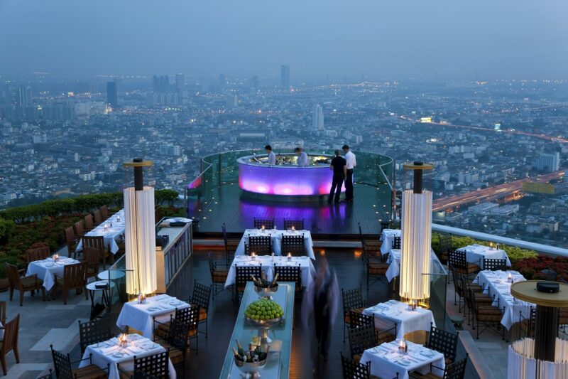 हो ची मिन्ह शहर में एक गगनचुंबी इमारत की छत पर स्थित रेस्तरां का उच्च कोण दृश्य, दूरी पर रोशनी से जगमगाता शहर का दृश्य।